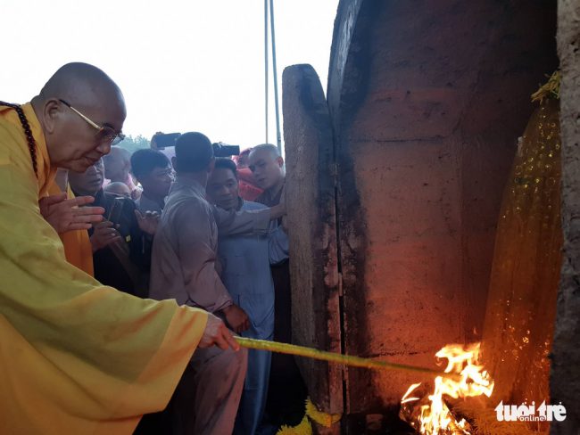 Một đại lão hòa thượng đưa ngọn lửa vào bên trong lò hỏa táng.