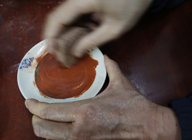 Màu đỏ tạo ra từ việc mài thỏi son trên lòng chiếc đĩa sành. Các bột này sau khi mài được trộn với nước và hồ bột nấu từ gạo nếp để tranh được bền màu.