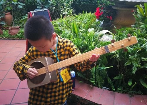 Chen Muyuan (8 tuổi, thành viên ban nhạc Tái chế) tập chơi đàn guitar được tái chế từ vỏ hộp bánh, bìa các tông.