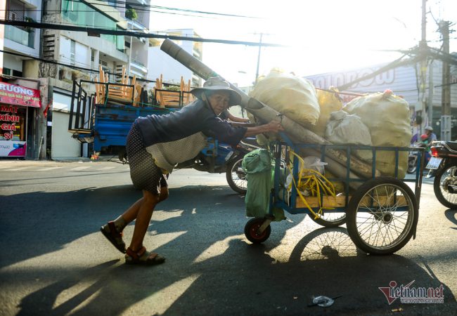 Giữa dòng xe xuôi ngược, bà Nguyễn Thị Mẫn còng lưng đẩy chiếc xe giấy vụn, lưng bà ngả theo bóng chiều nhưng miệng bà lúc nào cũng nở nụ cười tươi rói. Ở tuổi 70, bà Mẫn đã làm công việc thu mua ve chai gần trọn đời người. Hiện bà sống một mình trong con hẻm ở quận Bình Thạnh. Khó khăn kiếm sống từng đồng, được ngày nào ăn ngày nấy nhưng không lúc nào bà than thở.