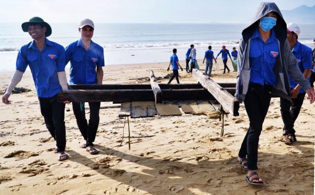 Các nam sinh cùng khiêng một khung gỗ bị sóng đánh dạt vào bờ. "Lượng rác thải rất lớn nên chúng tôi chủ động phân công, nữ sẽ nhặt rác cho vào túi, còn nam sẽ kéo rác ra ngoài nơi tập kết", sinh viên Nguyễn Thành Tân nói.