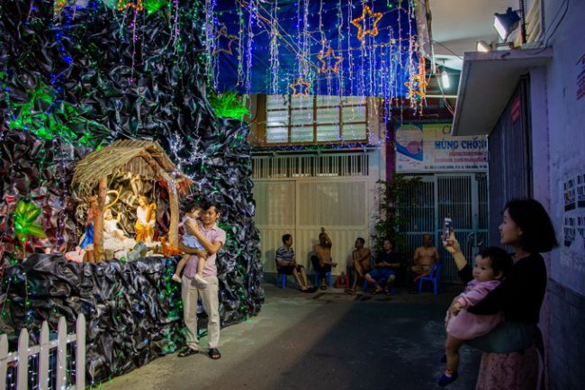 Dưới những chùm đèn màu, một gia đình tham quan và chụp hình tiểu cảnh mừng Chúa hài đồng trên đường Đất Thánh (quận Tân Bình).